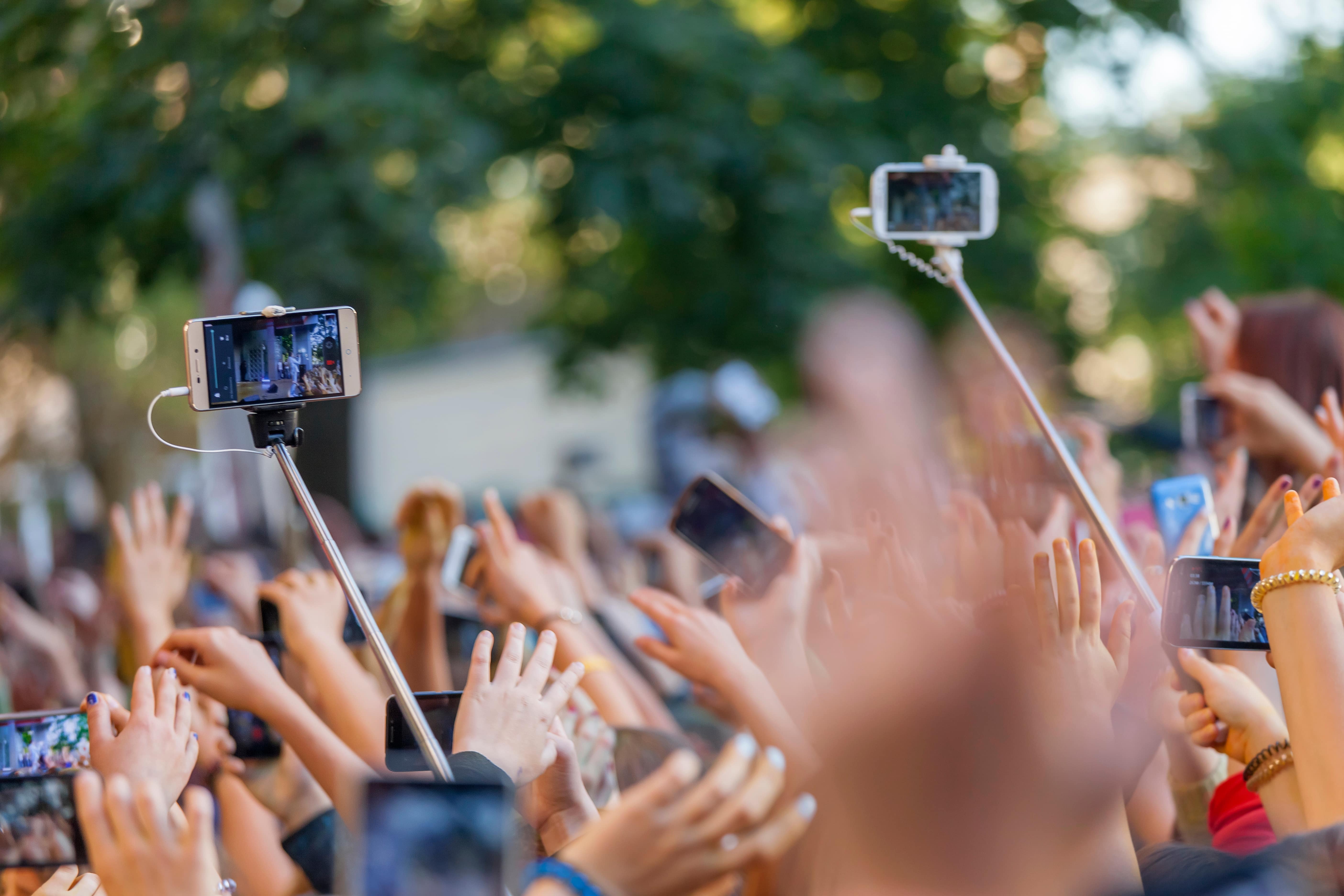 Tienda de accesorios para celulares, personas sosteniendo telefonos con selfie stick en festival de música.